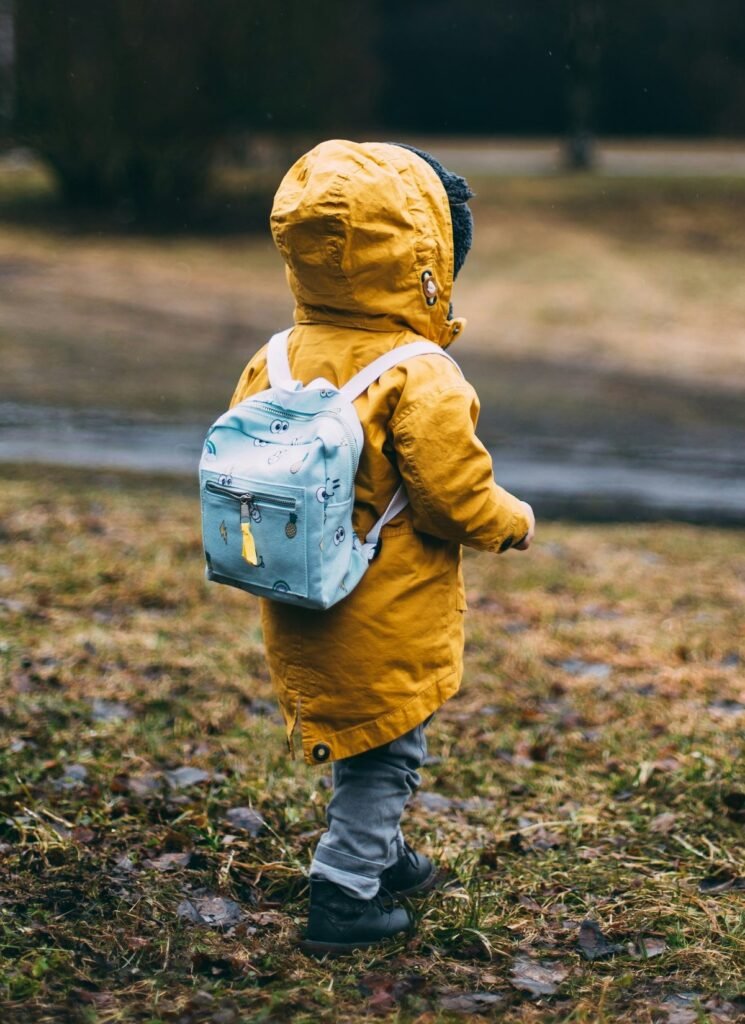 Toddler in yellow raincoat wearing a light blue backpack while walking outdoors