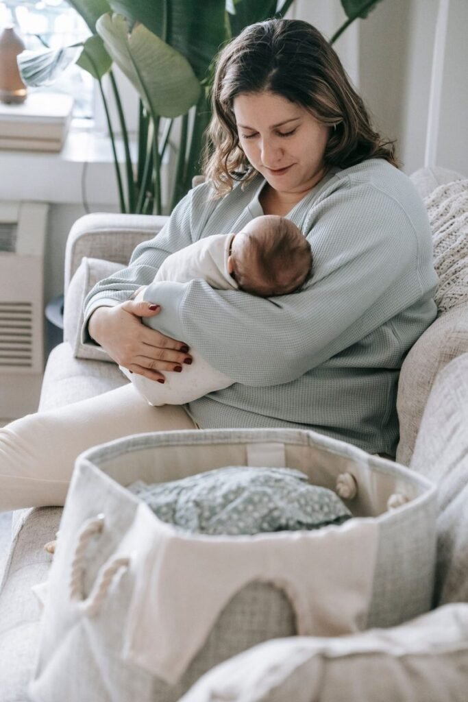 A mother cradles her sleeping newborn on the couch during the first month of breastfeeding.