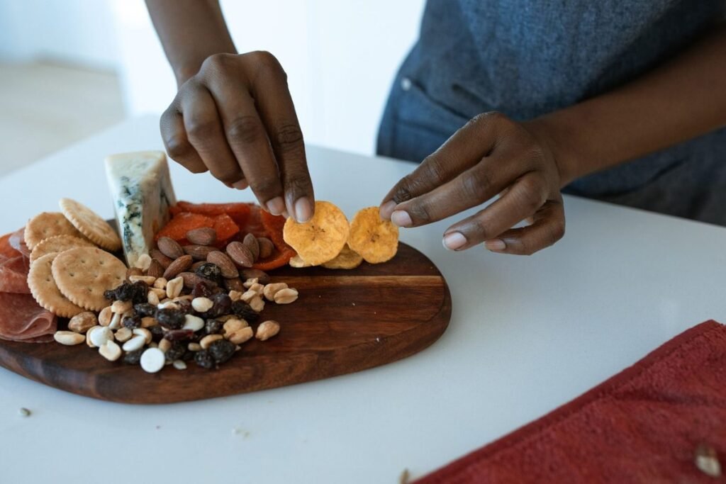 A hand picking healthy snacks like cheese, crackers, and dried fruit from a snack board.