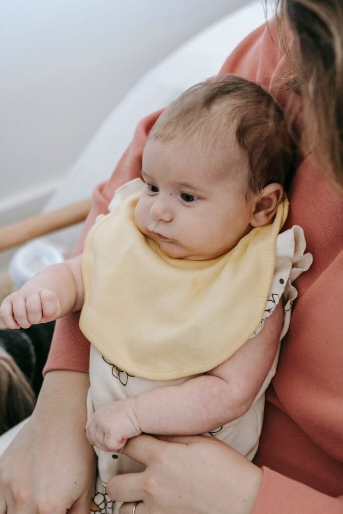 A mother holding her baby in a yellow bib while sitting comfortably.