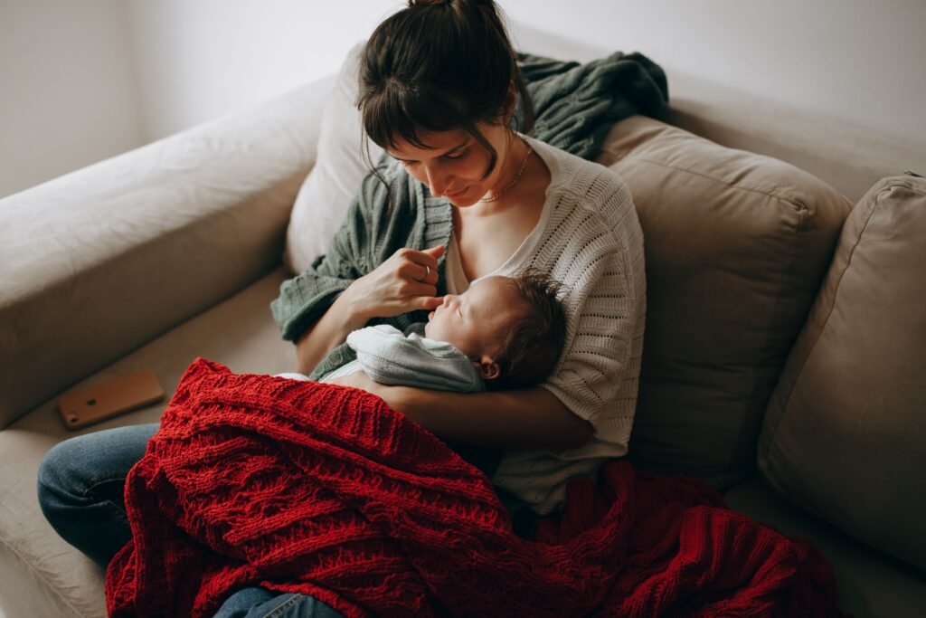 A new mom quietly nurses her newborn while wrapped in a red blanket, lost in thought.