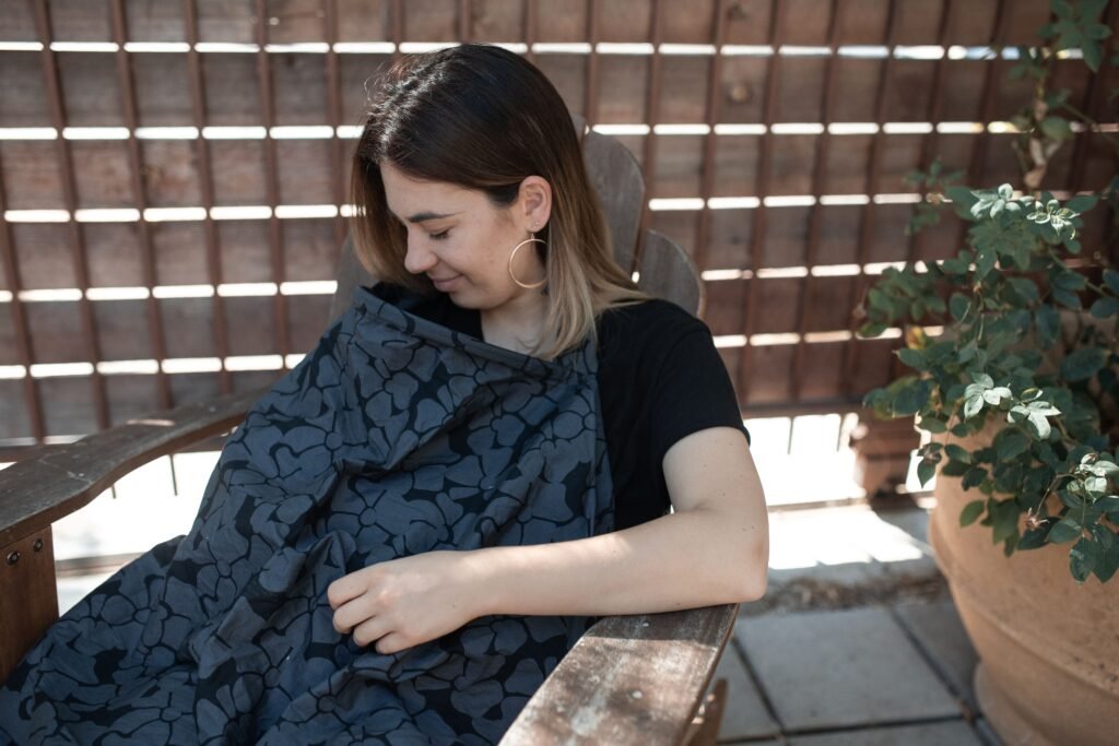 Mother nursing her baby outdoors under a cover on a patio, feeling confident about breastfeeding in public