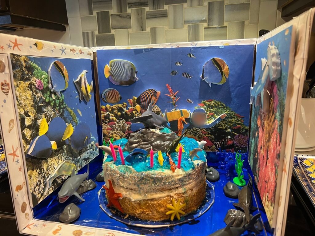 Custom under the sea diorama birthday cake with sharks, tropical fish, and a coral reef backdrop by Honey’s Baking Company